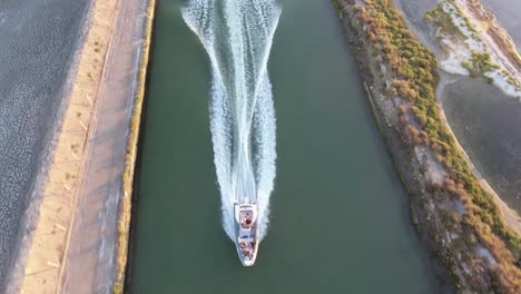 Vista-Vertical-Aérea-De-Drones-Siguiendo-Un-Barco-Rápido-En-Un-Canal-Durante-La-Puesta-De-Sol.